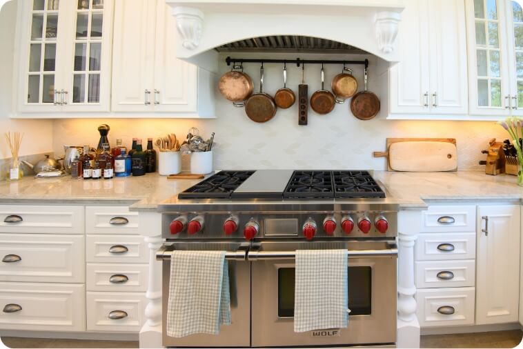 A modern kitchen featuring a stainless steel Wolf range, hanging pots, and elegant cabinetry.